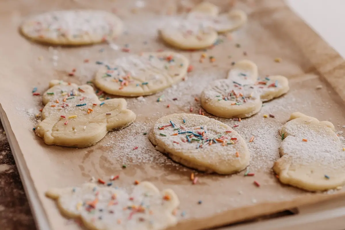Raw cookies with sprinkles on baking parchment, ready to be baked.
