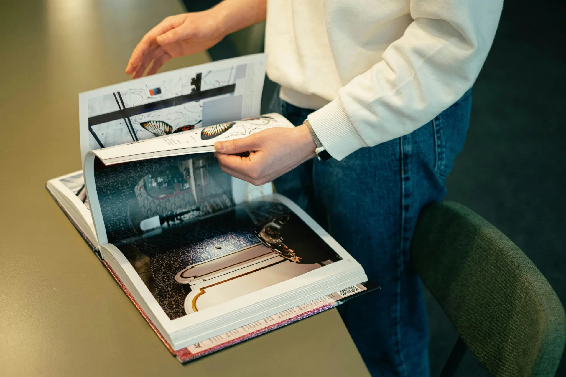 Person looking at an art magazine placed on a table.