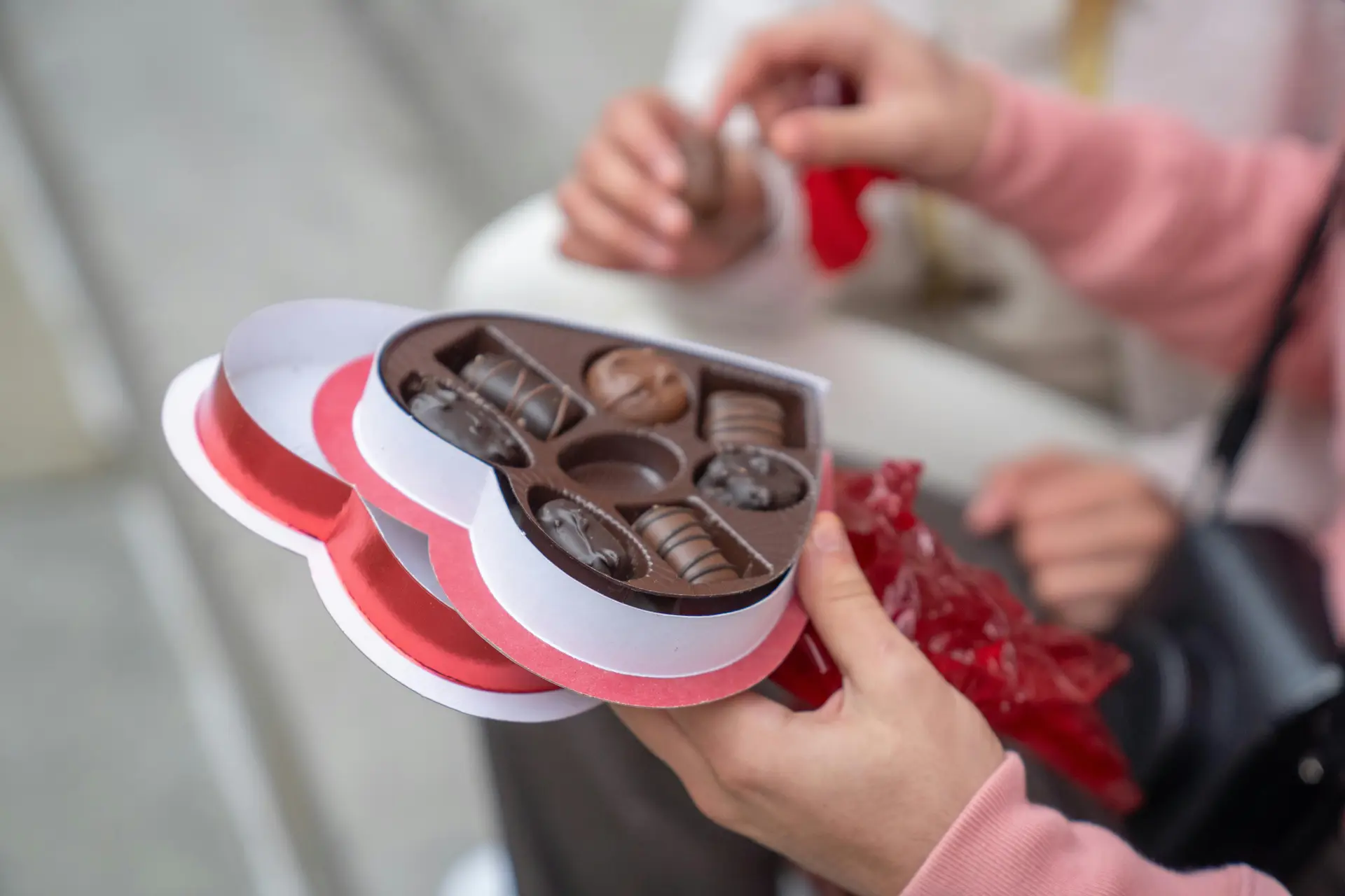 A person holding a heart shaped chocolate box. There are some chocolate in the box.