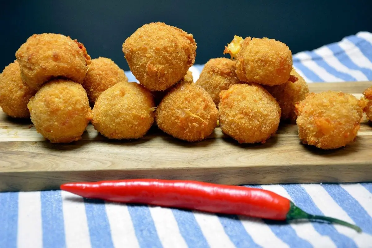 Fried cheese curds on a wooden plate along with a red pepper.