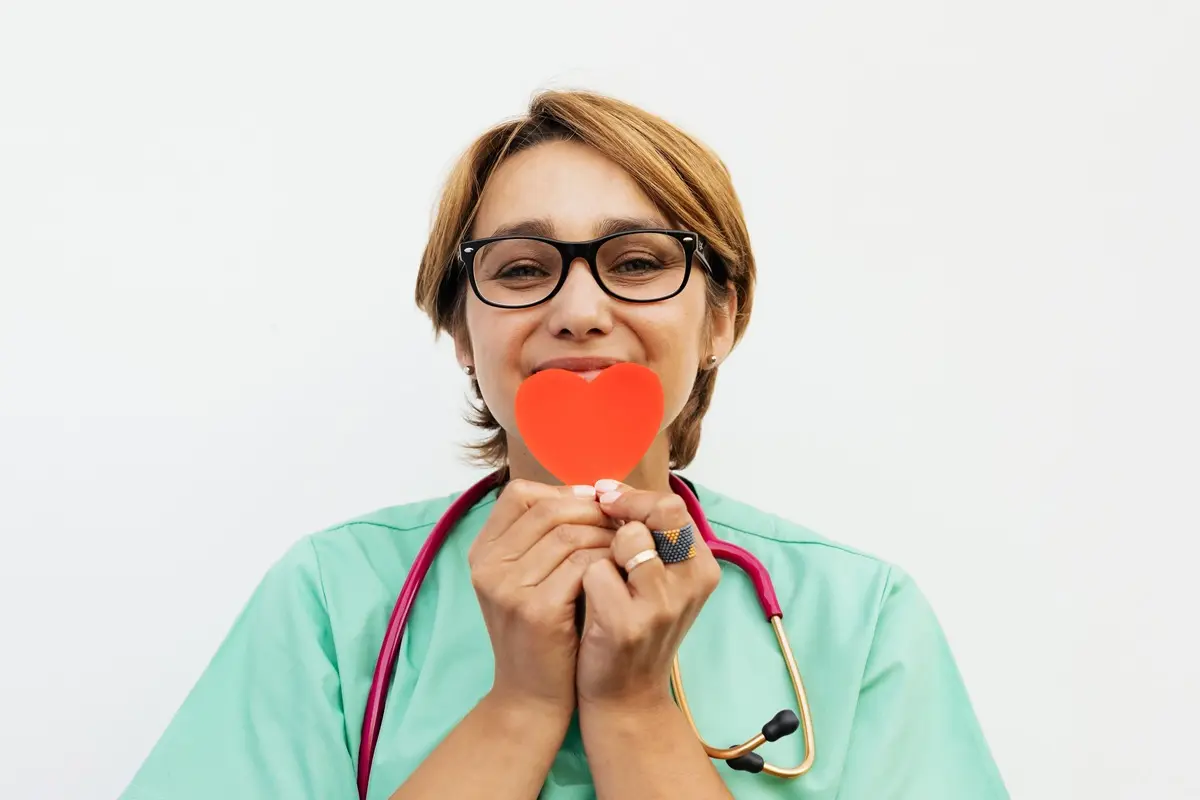 A nurse holding a red heart symbol, promoting healthcare compassion.