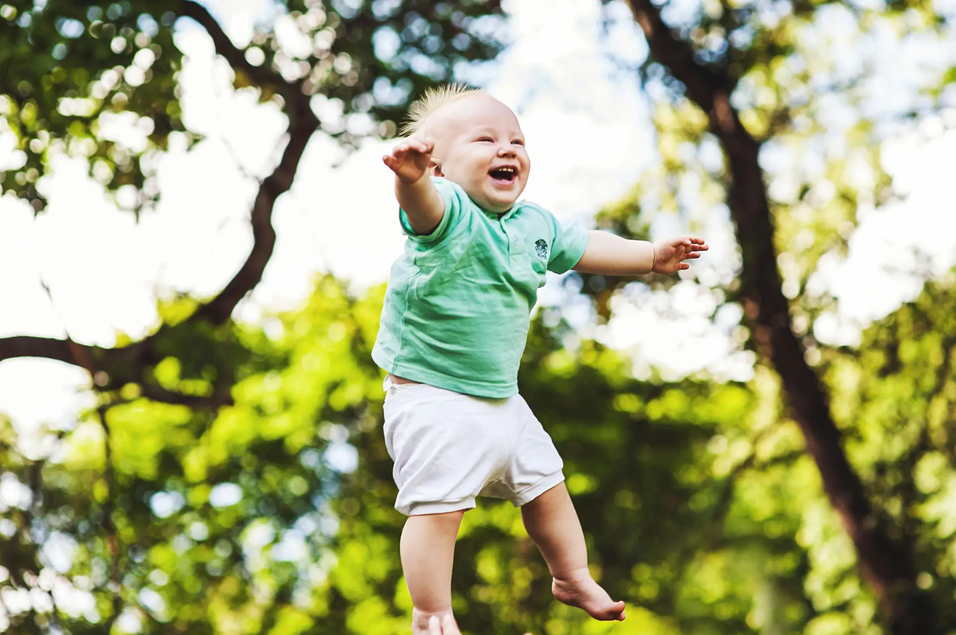 Laughing baby floating in the air, perhaps its thrown up by his parents in a playful manner.