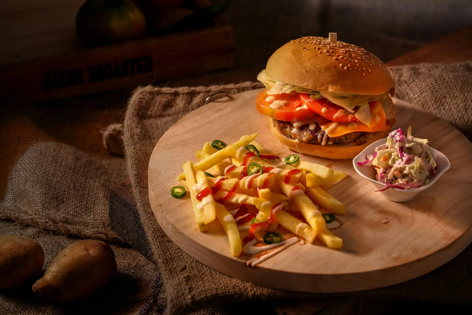 Cheeseburger on a wooden plate along with some fries and toppings.