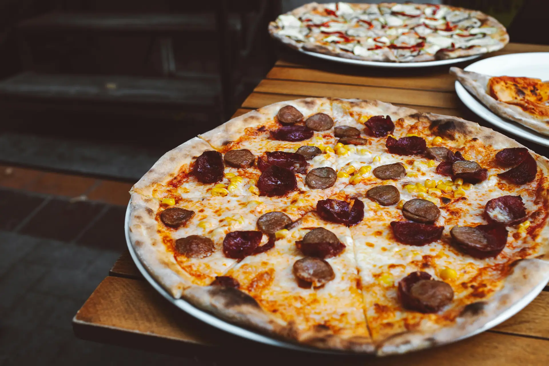 Sausage Pizza with dark meaty sausages on a wooden table with other dishes.