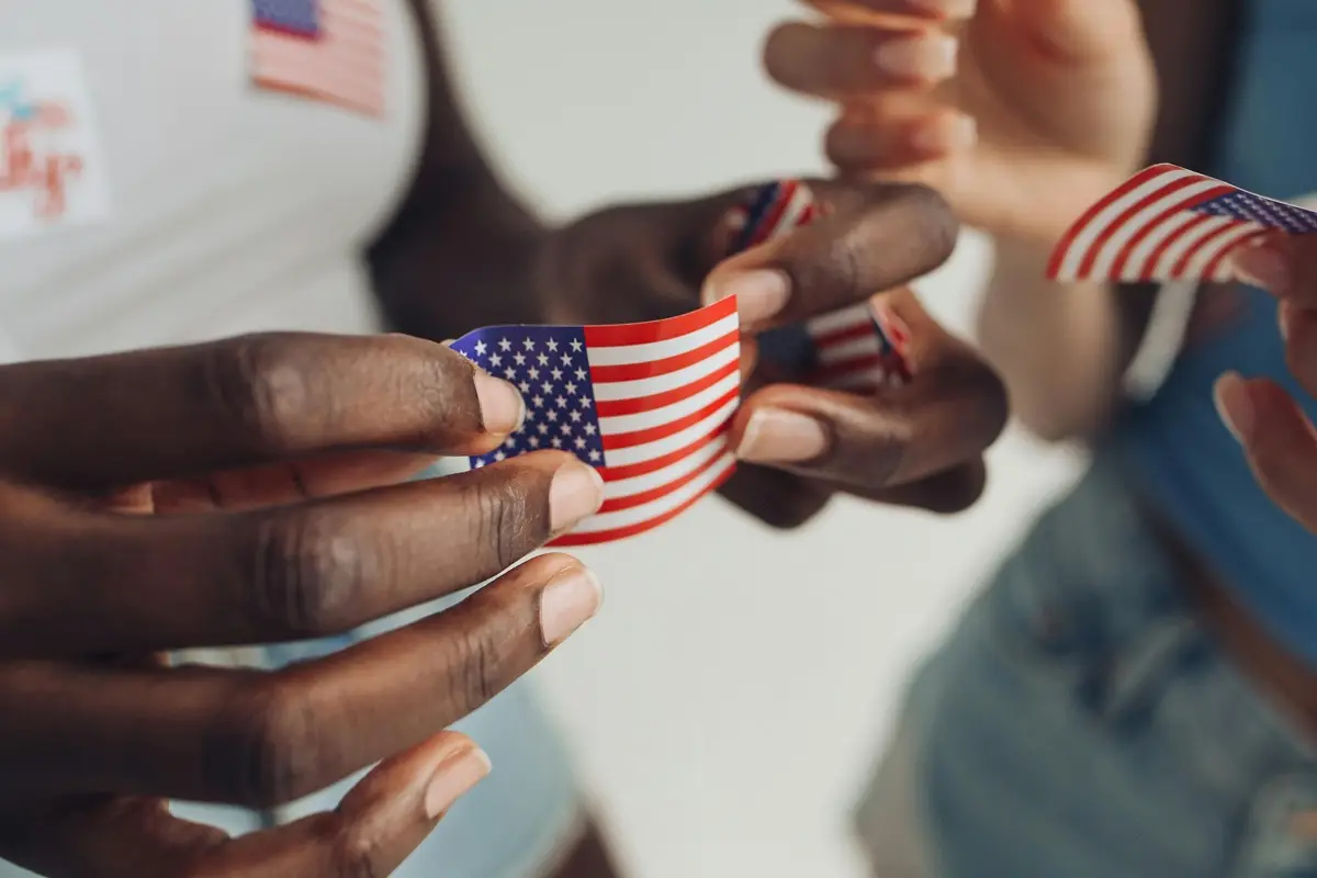 Close-up of diverse hands holding USA flag stickers, symbolizing unity and patriotism.