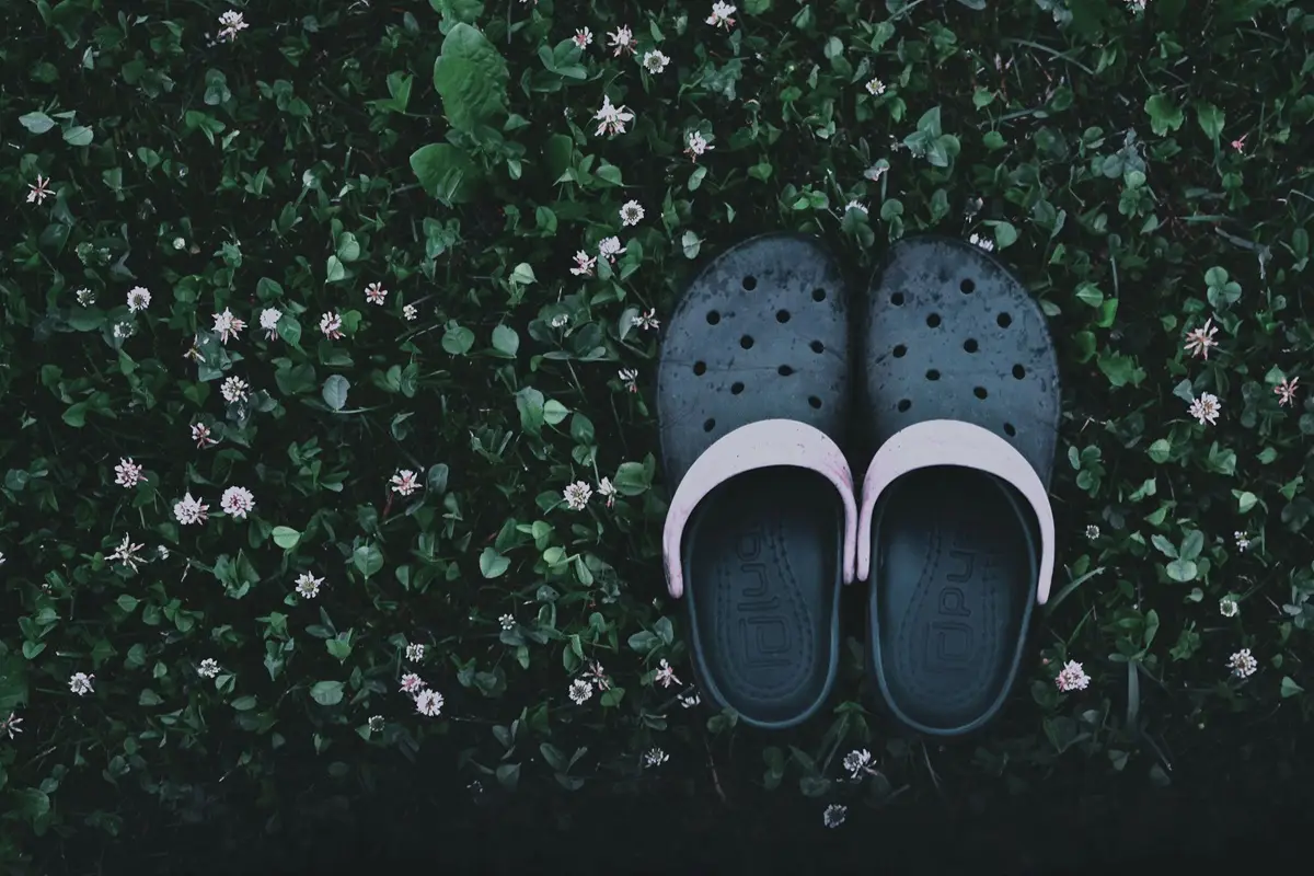Overhead shot of casual clogs on a lush grass bed with small flowers.