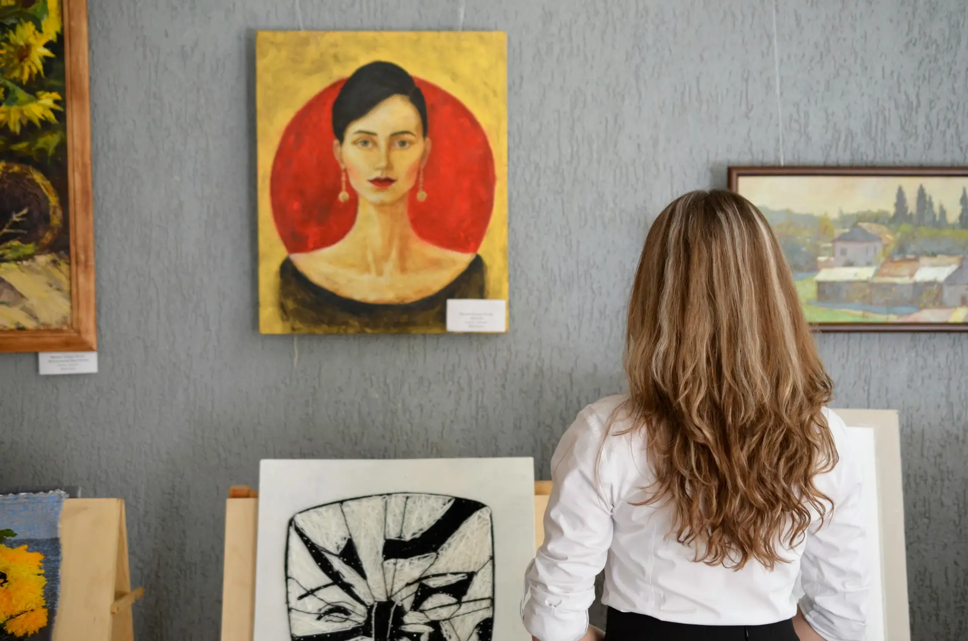Woman looking at paintings displayed on the wall.