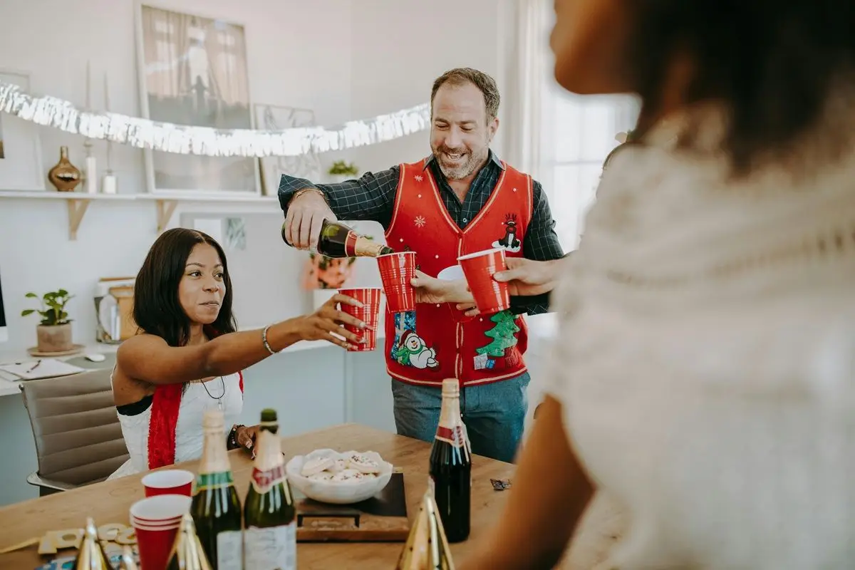 A person pouring a drink in a Christmas party while wearing a ugly red holiday sweater.