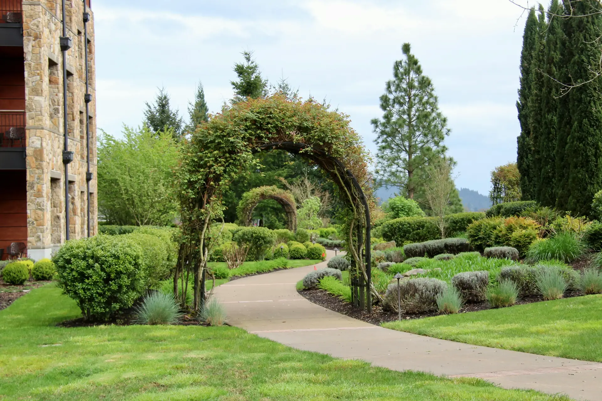 A beautiful public garden with green arch in the middle and bushes and trees on the sides.