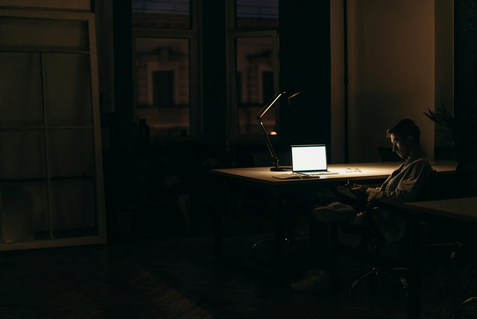 A person sitting in a dimly lit room with a laptop on the table.