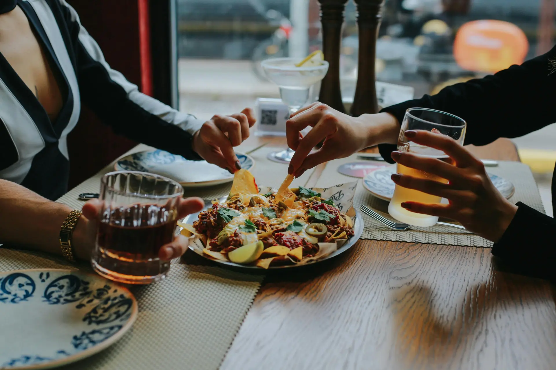 Two person enjoying a plate of nachos while drinking orange juice.