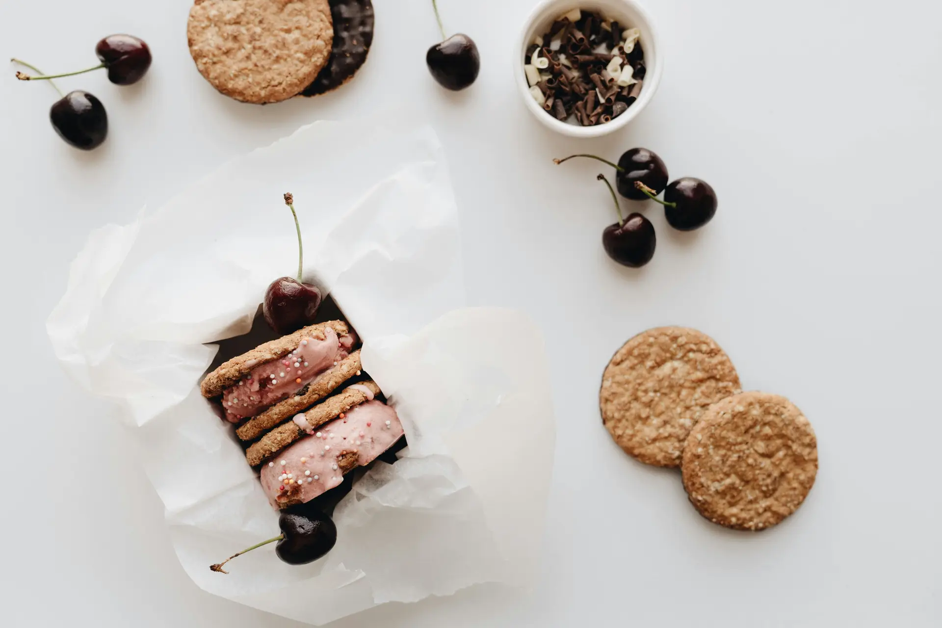 Ice cream sandwich with berries on a white table. There are some cookies as well.