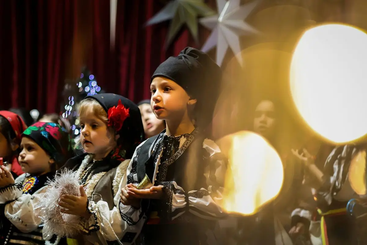 Children dressed up singing Christmas Carol on a stage.