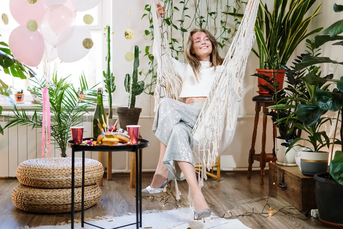 A young woman relaxes in a hammock surrounded by plants and party decorations.