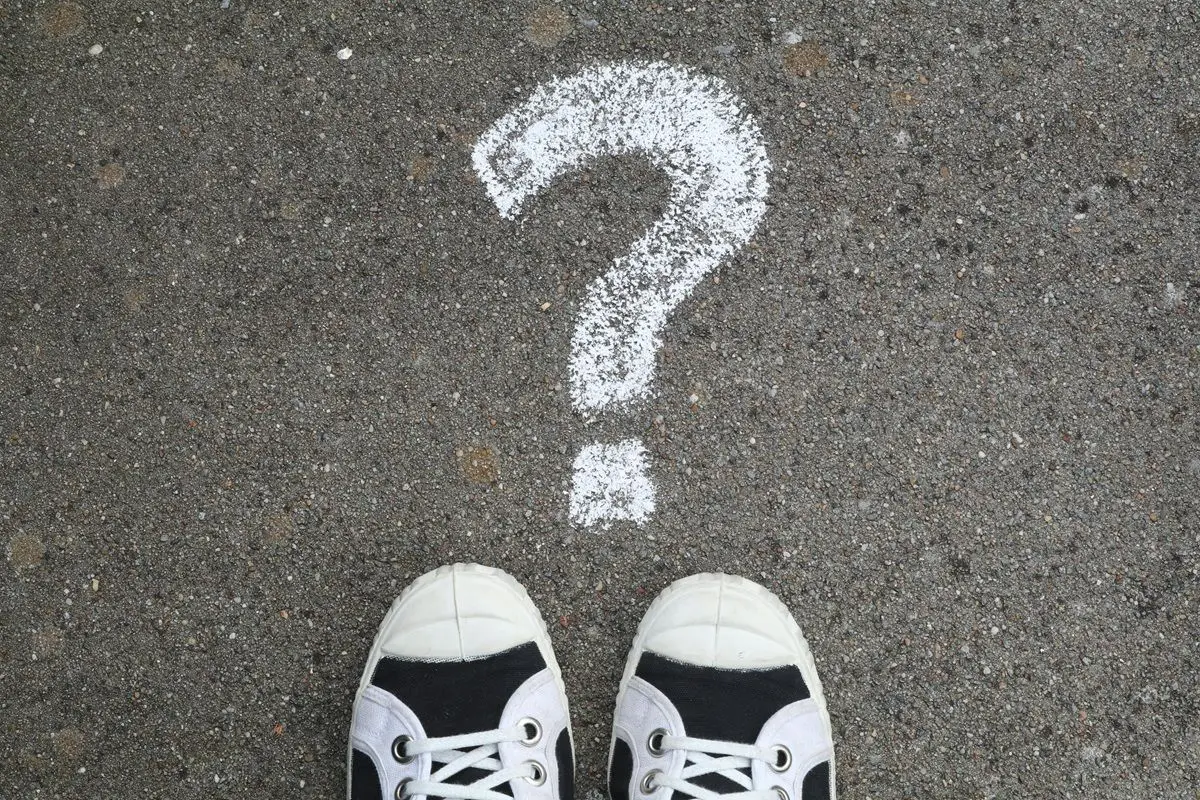 Two pair of shoes on the street. There's a question mark painted near the shoes.