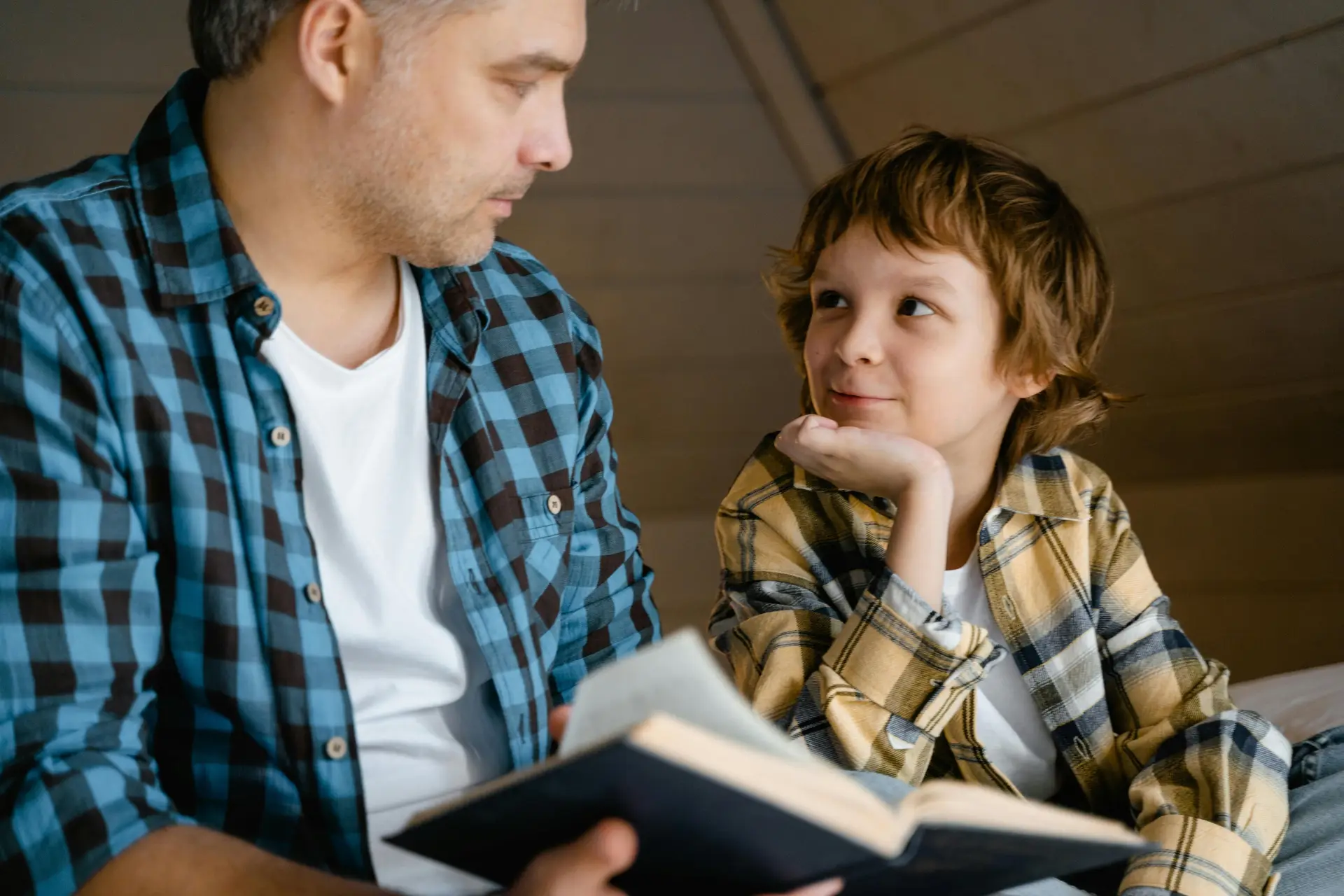A Boy Looking at the Man Holding a Book and telling story.