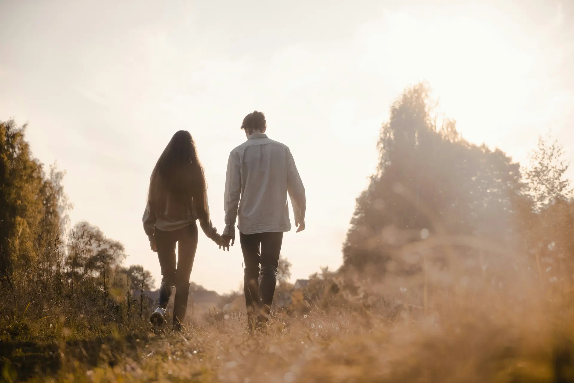 A couple walking while holding hand. The setting sun is in front of them.