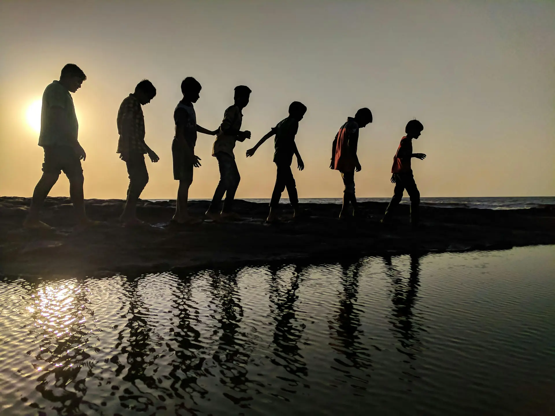 silhouette of a group of children walking near body of water.