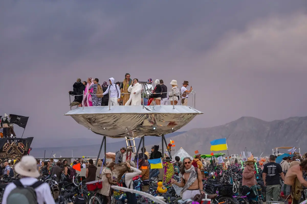 Colorful festival with people in costumes on a UFO art installation outdoors.