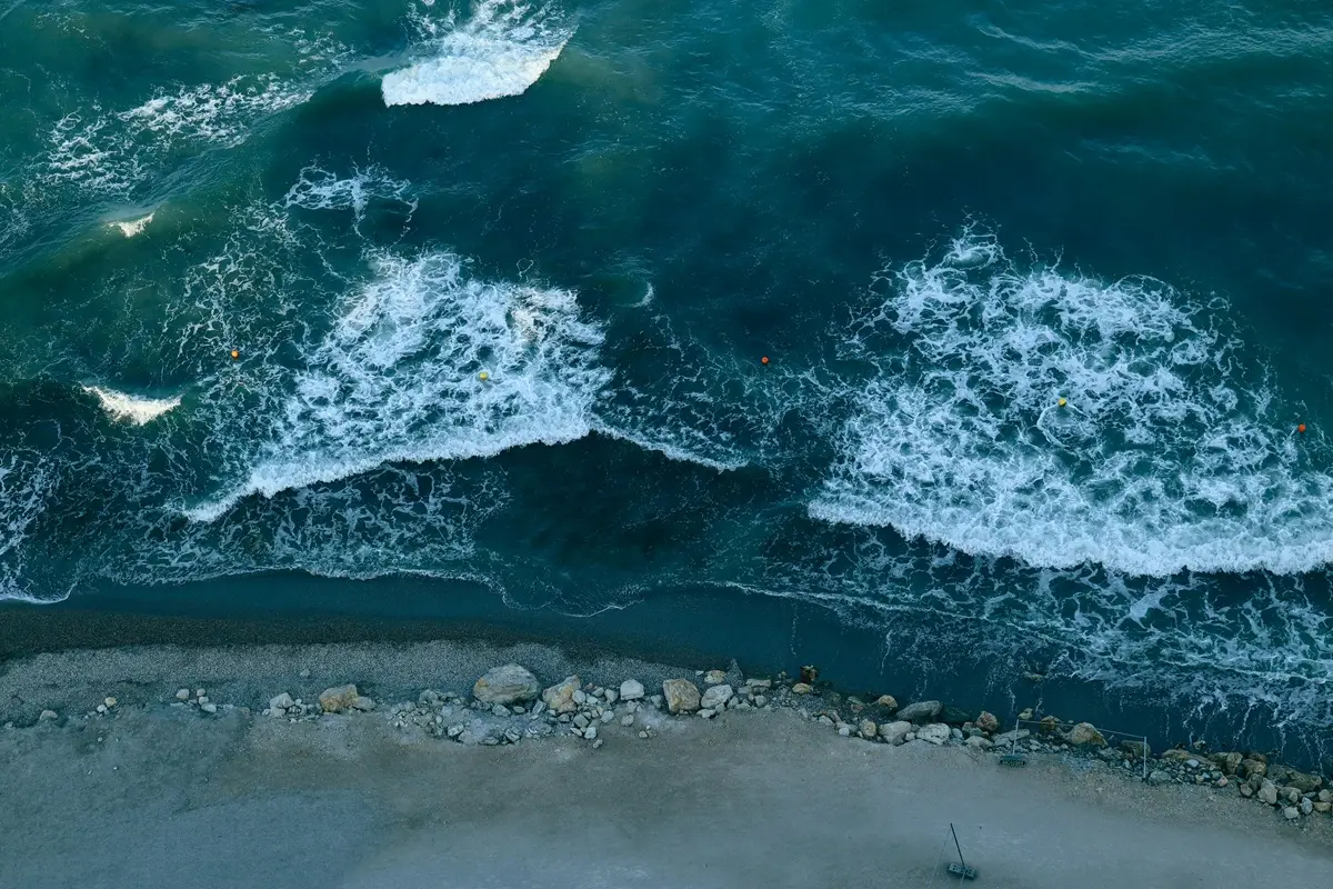 Aerial shot of ocean waves crashing against a rocky shoreline, creating beautiful foam patterns.