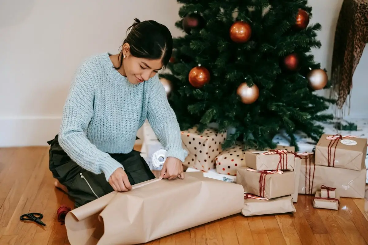 A person wrapping gifts with brown wrapping paper. There are some gifts under the tree that they are wrapping present under..