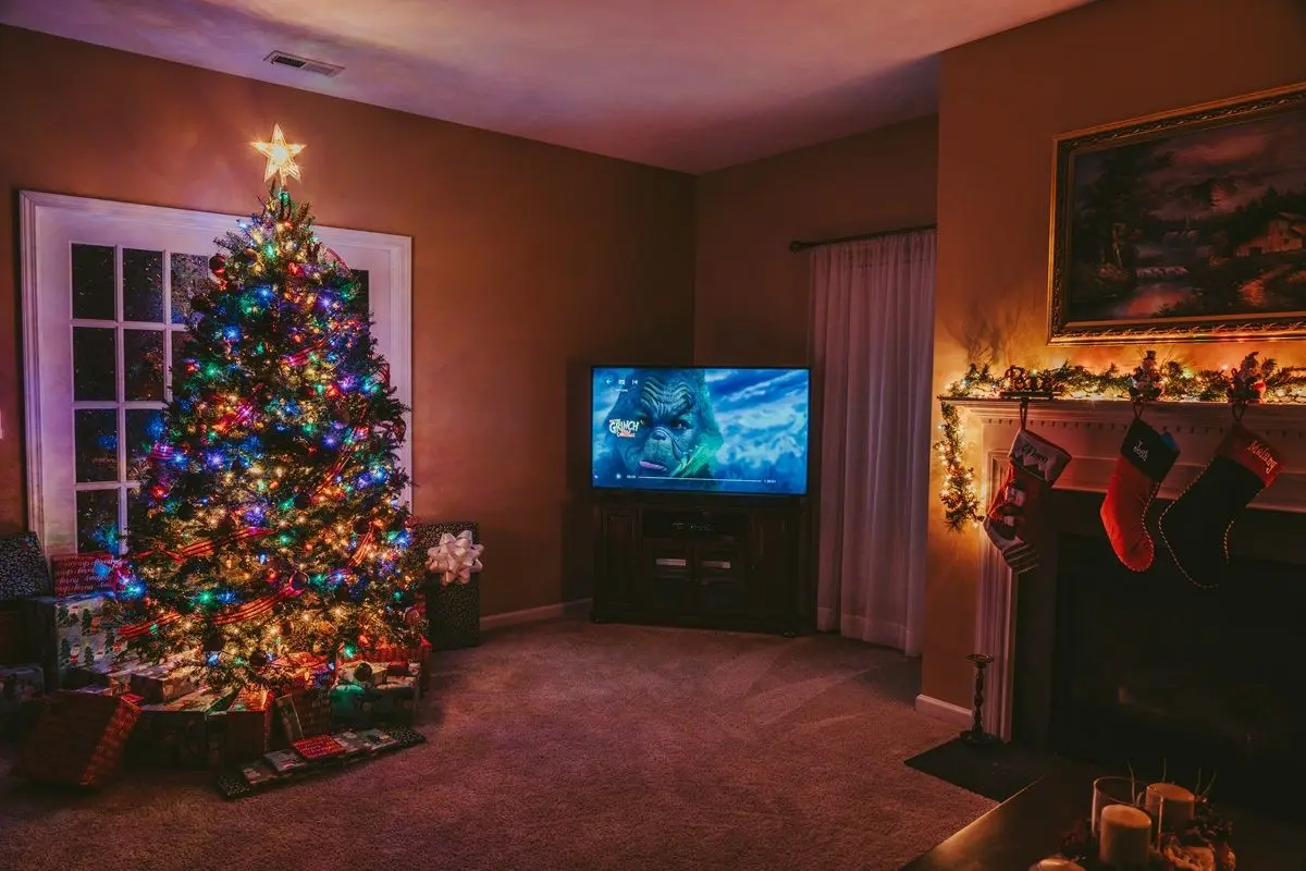 A cozy living room with a Christmas tree, tv playing The Grinch, and a fireplace.