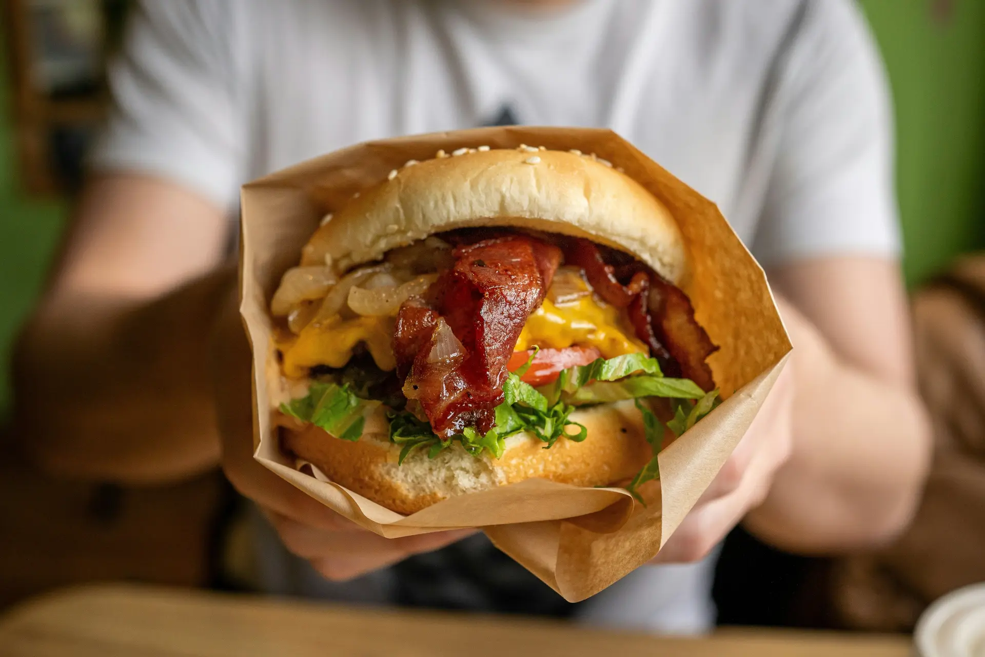 A person holding a cheeseburger wrapped in a paper bag.