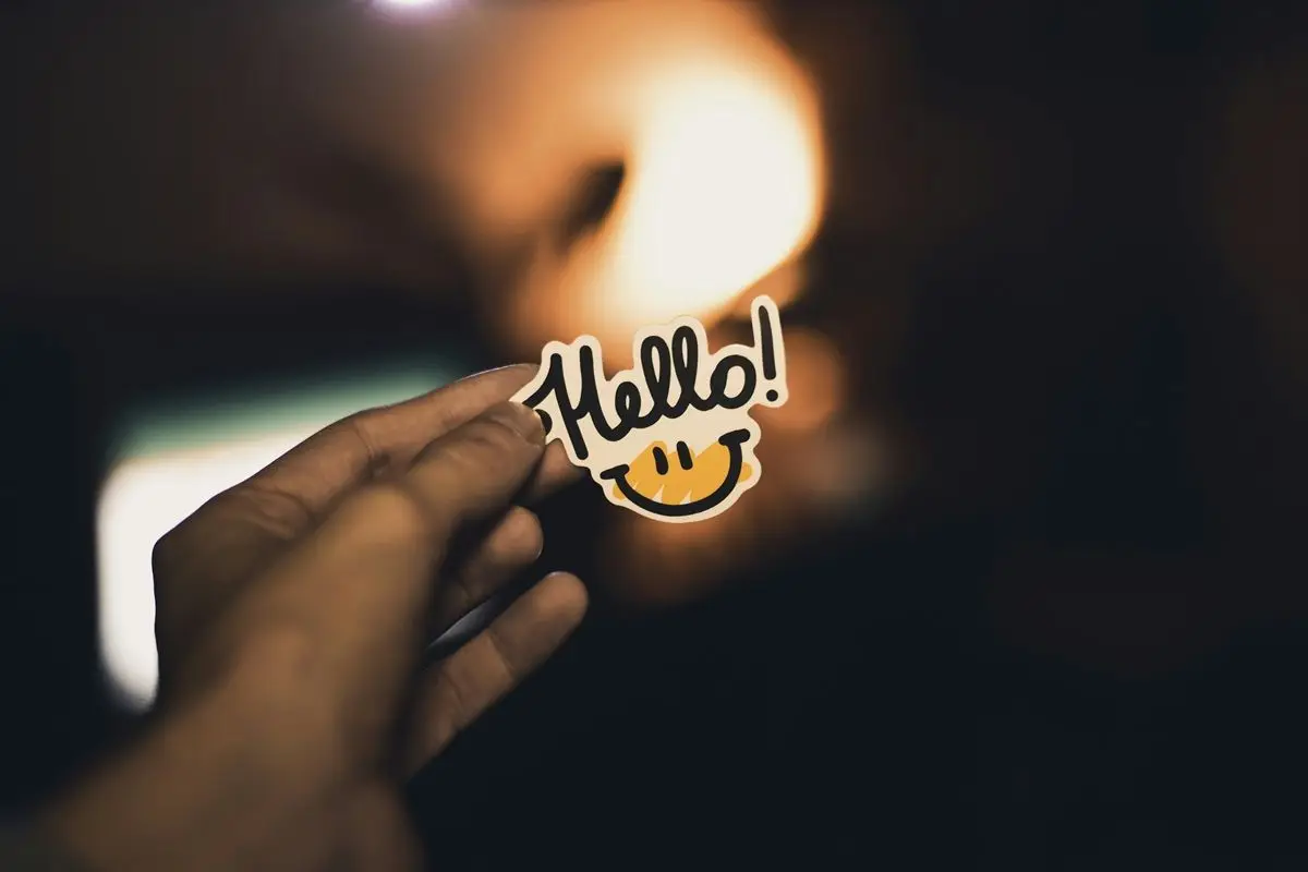 A person holding a sticker that has the word hello and a smiley face on it.