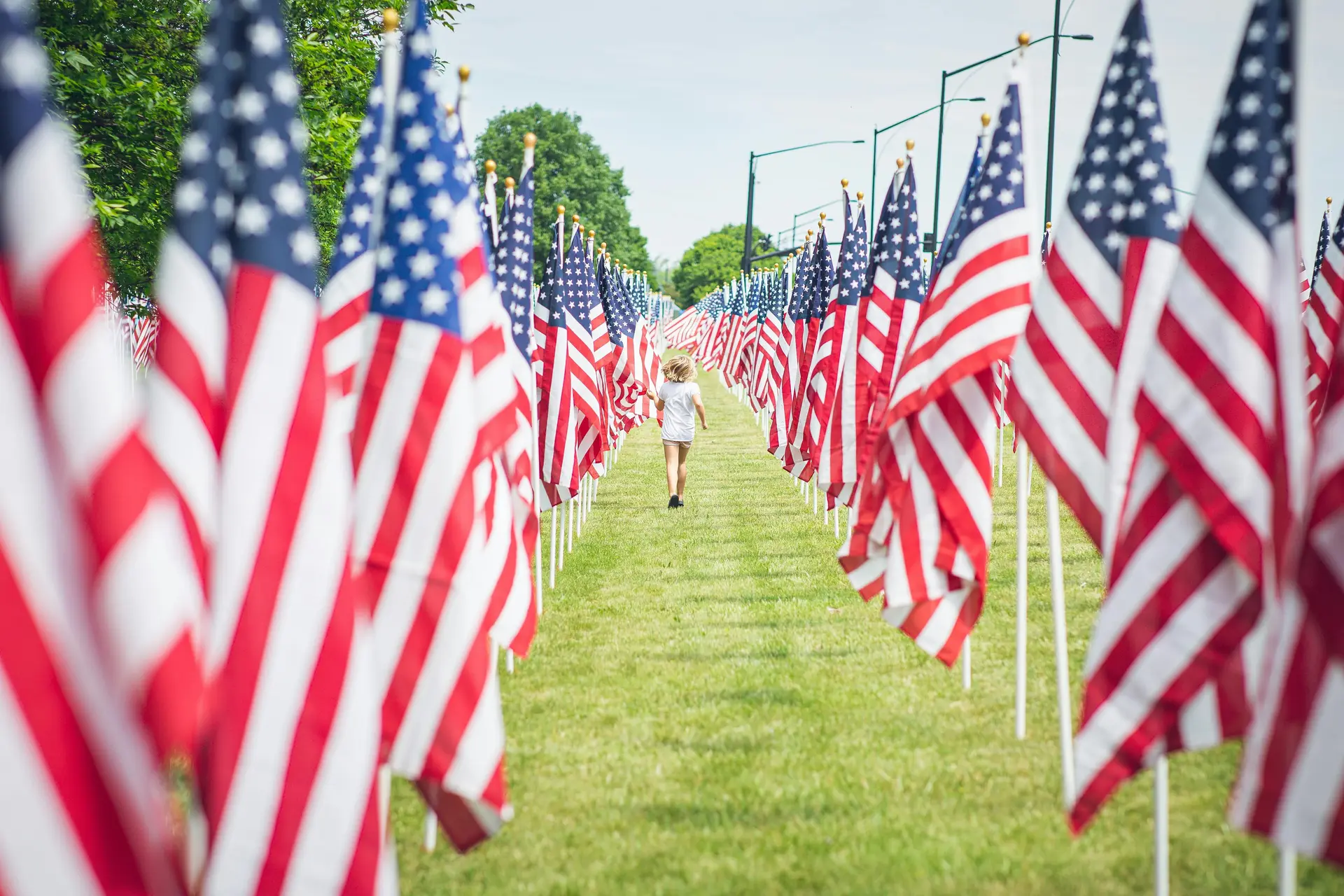 A child walks through a corridor of half staffed USA flags.