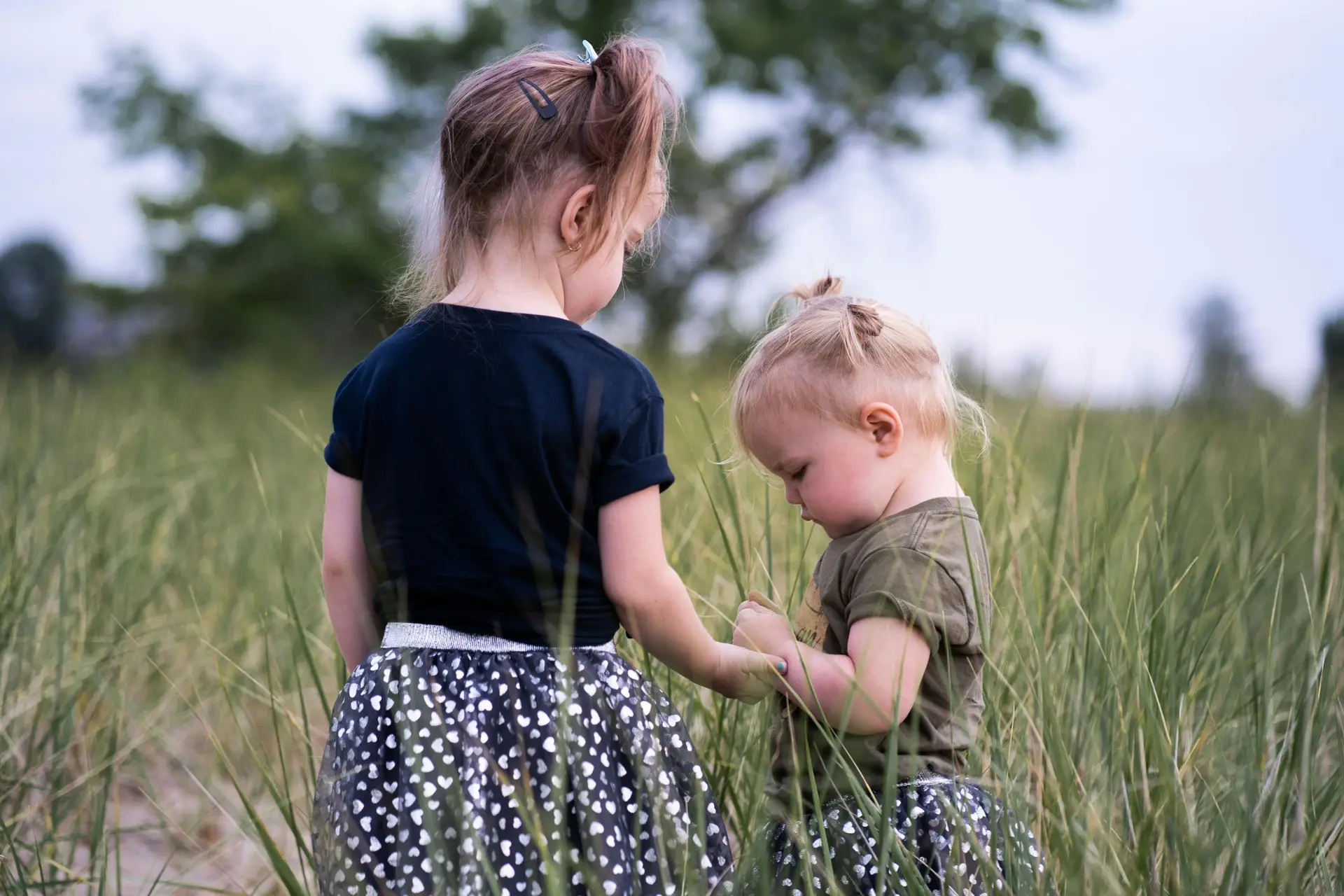 Two child playing in a grass field.