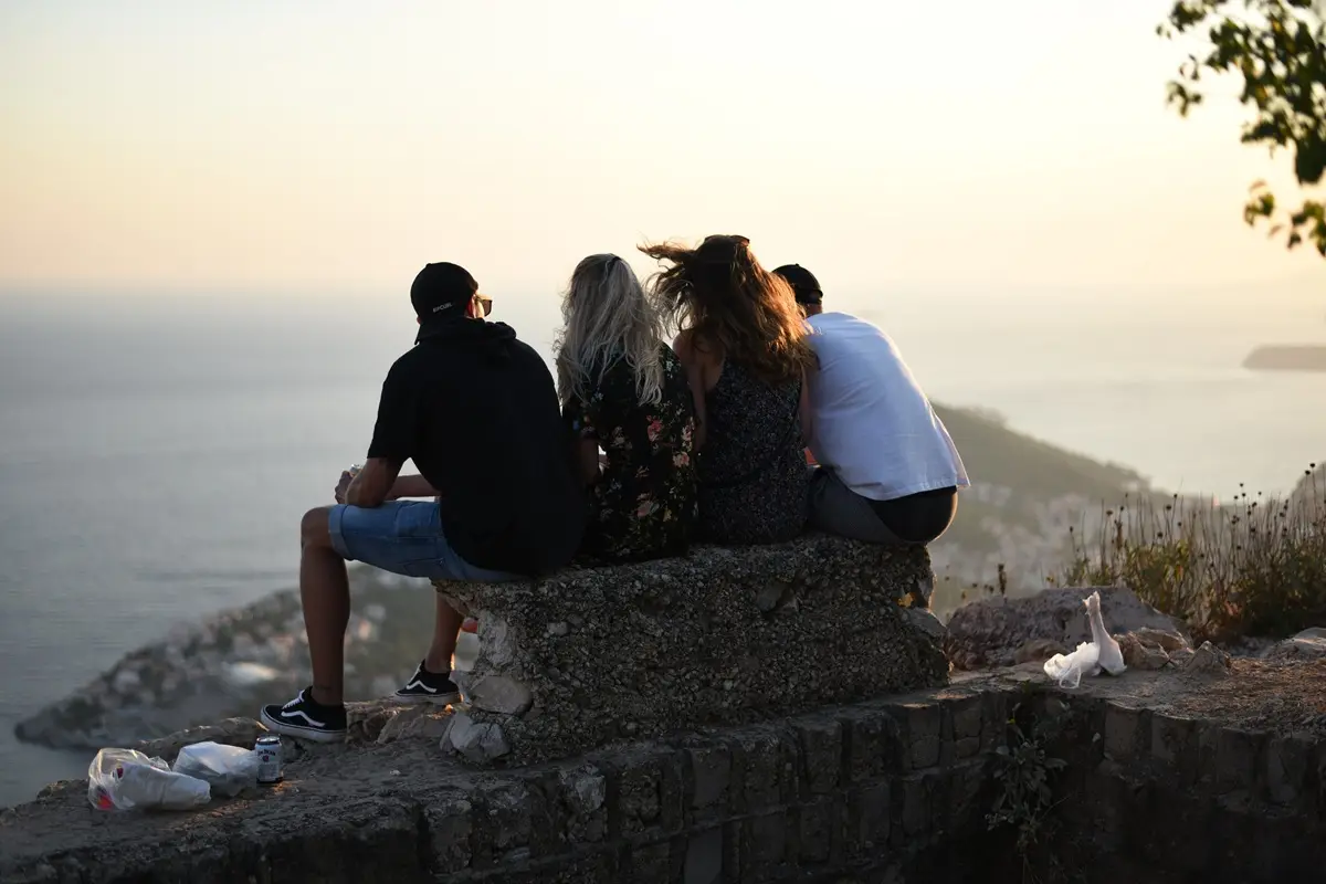 A group of friends sitting on a stone wall, enjoying a scenic sunset view by the sea.