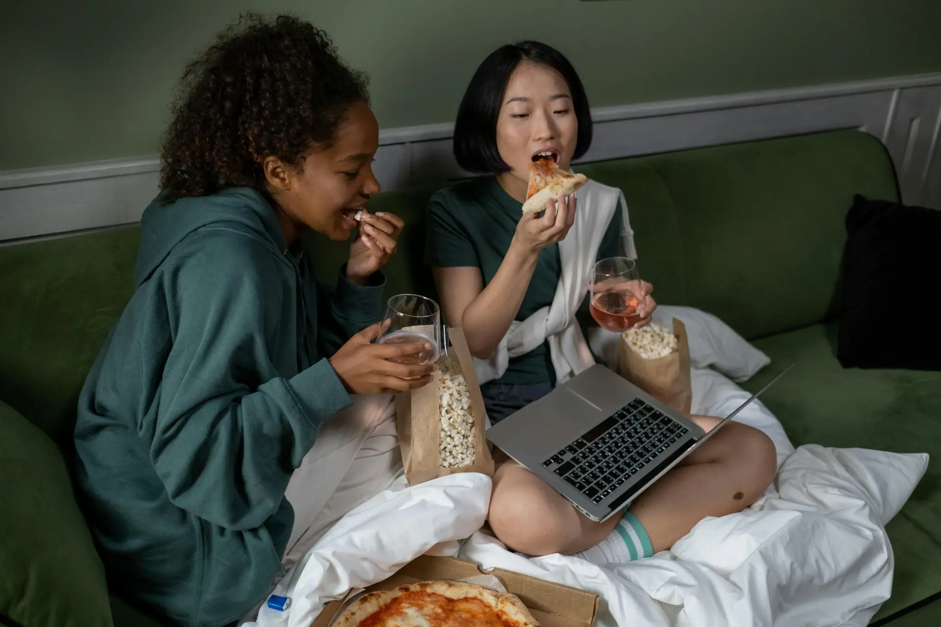 Two women eating pizza and watching movie on their laptop.
