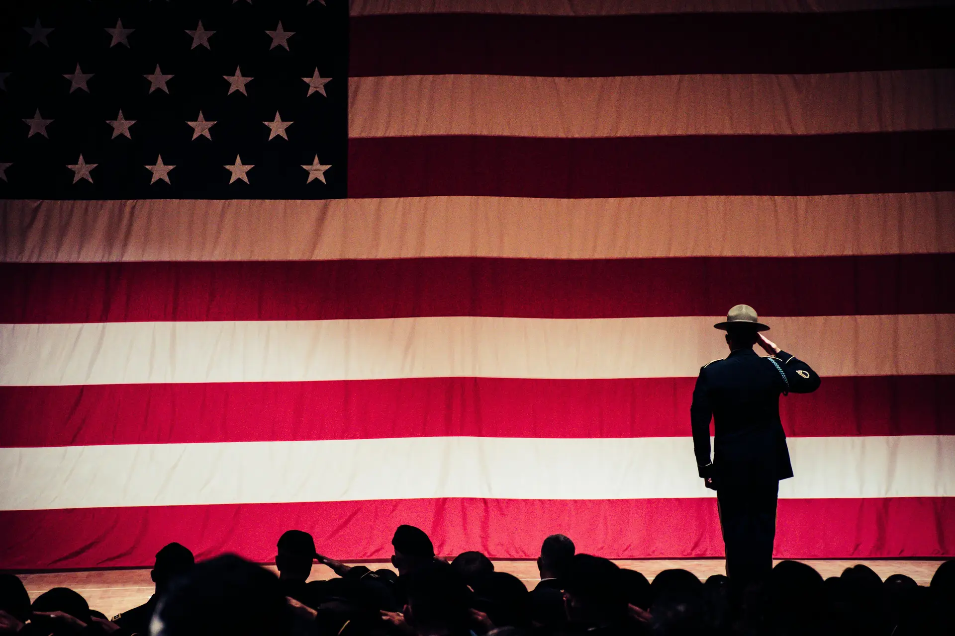 A person saluting the Flag of america. There are bunch of other peoples near him who are saluting as well.