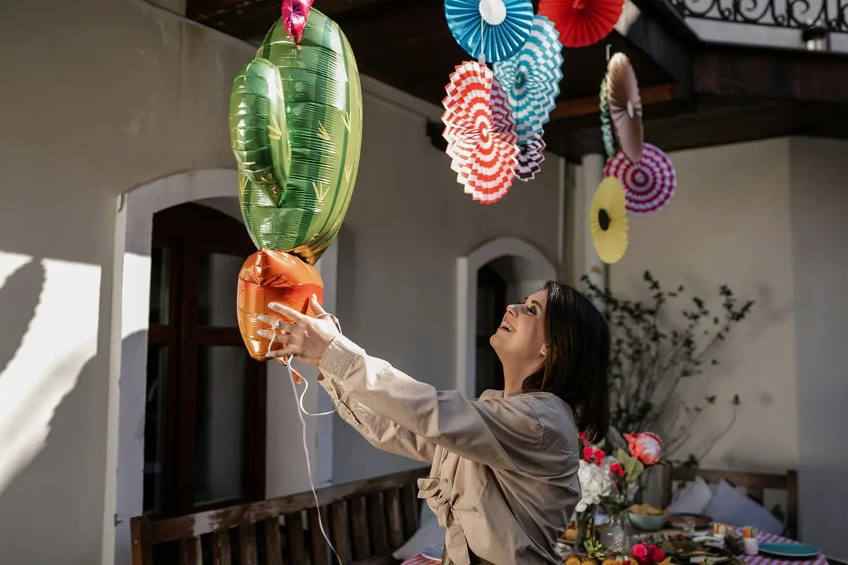 A person holding a cactus shaped balloon while laughing.