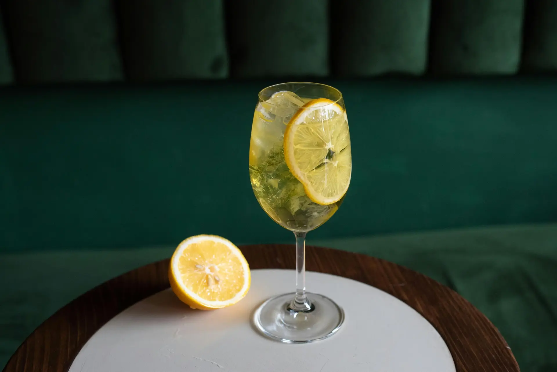 Lemon juice in a wine glass along with two slices of lemon. There's another sliced lemon near the glass.