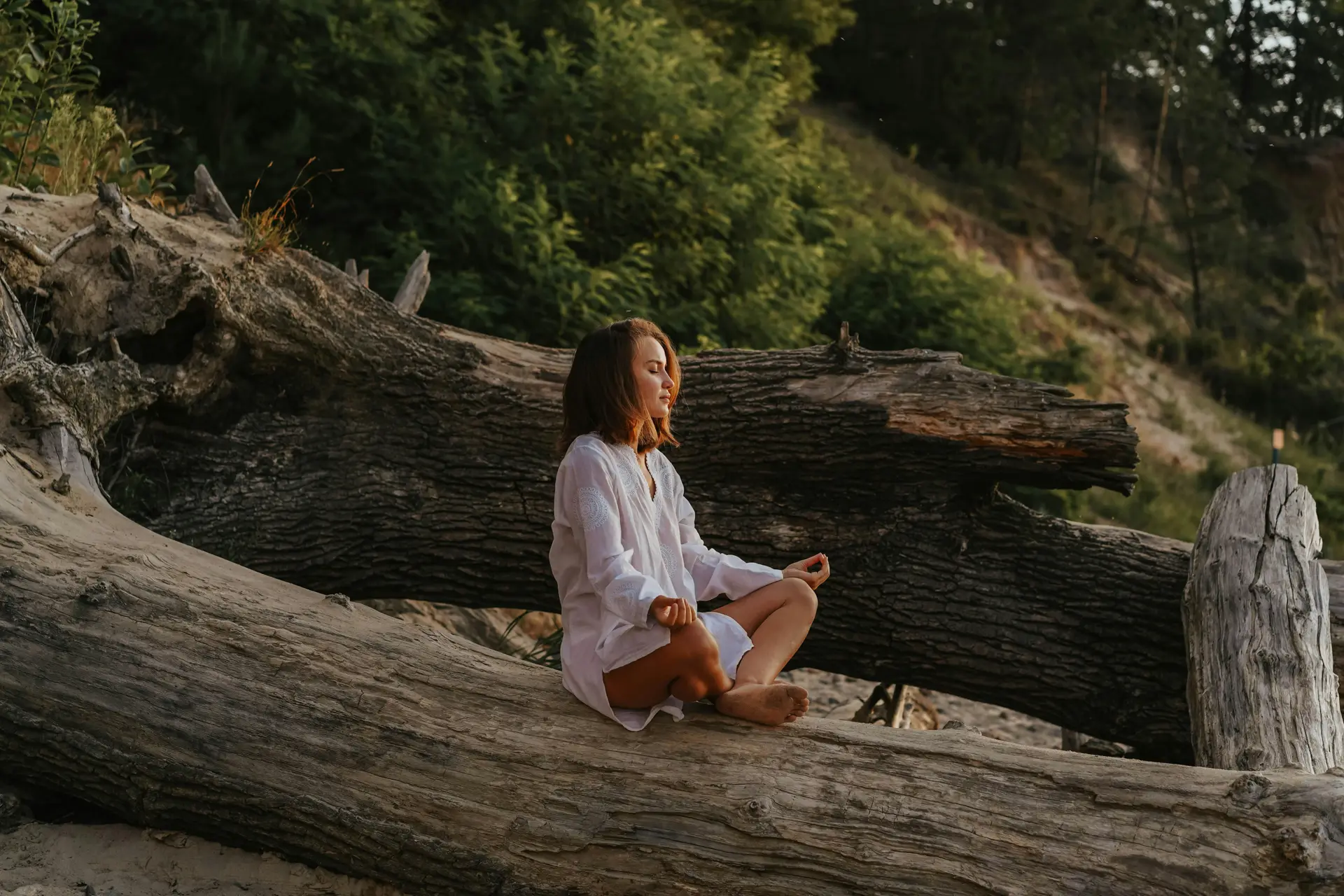 A woman meditating on a fallen tree.