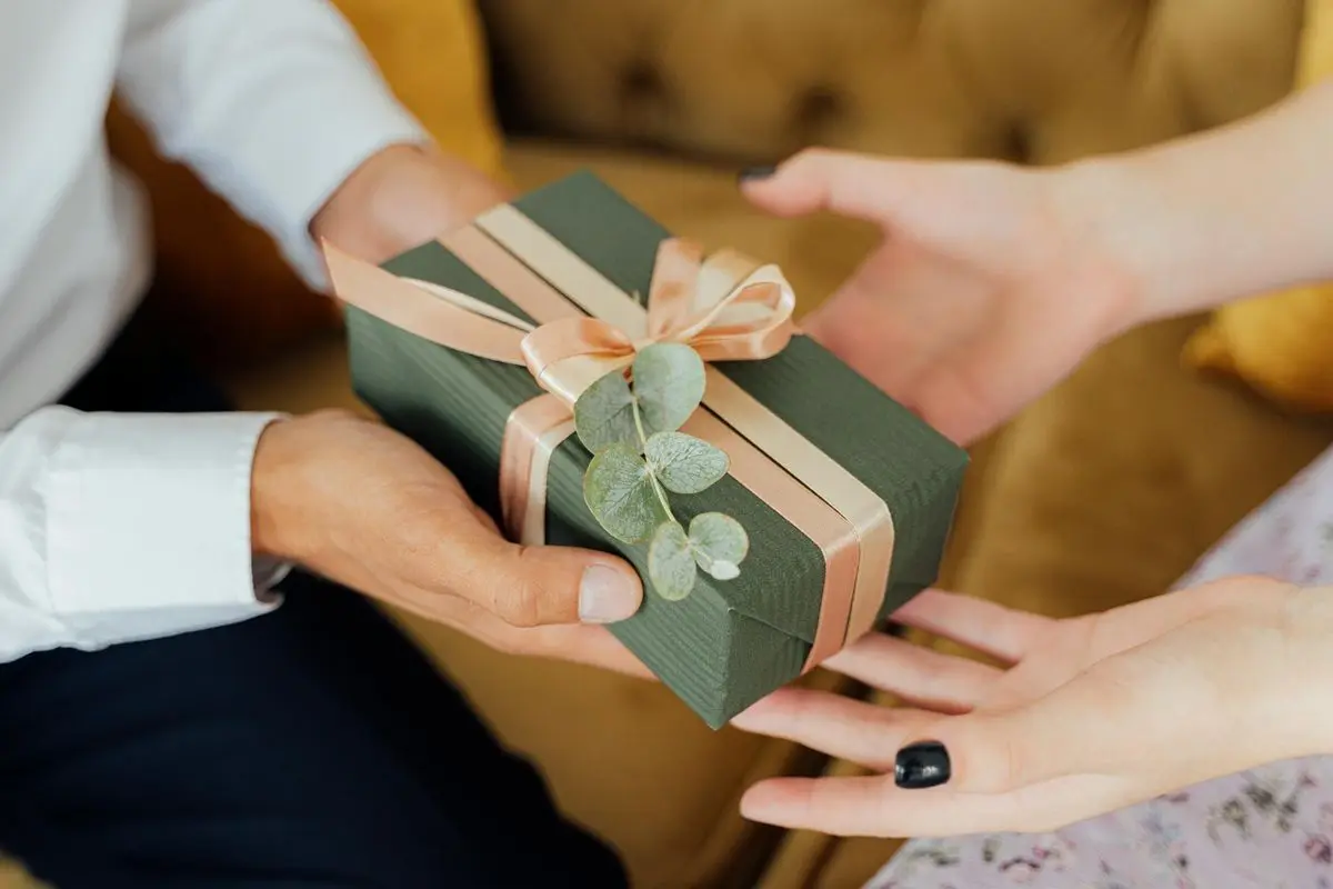 A person giving another person a giftbox that has a ribbon on it.