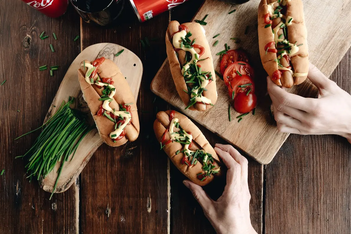 Delicious hot dogs topped with fresh chives and tomatoes on a rustic wooden board.