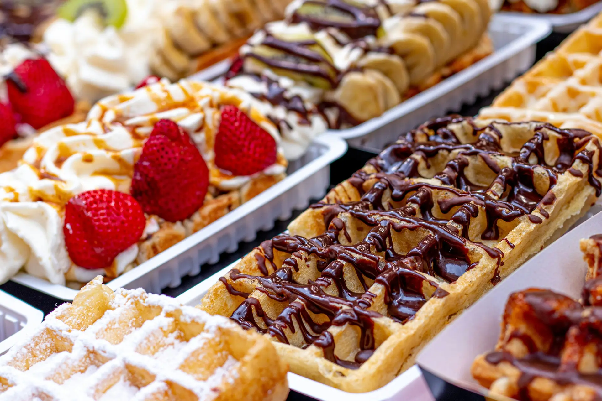 Many waffles on display with different types of toppings, including chocolate, strawberry, and icecream.