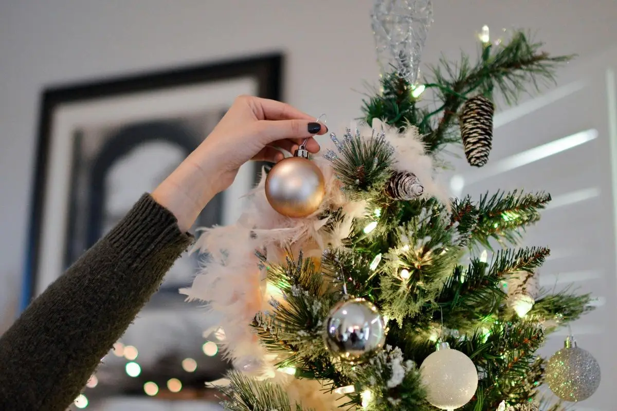 A person putting a bauble on a lit Christmas tree.