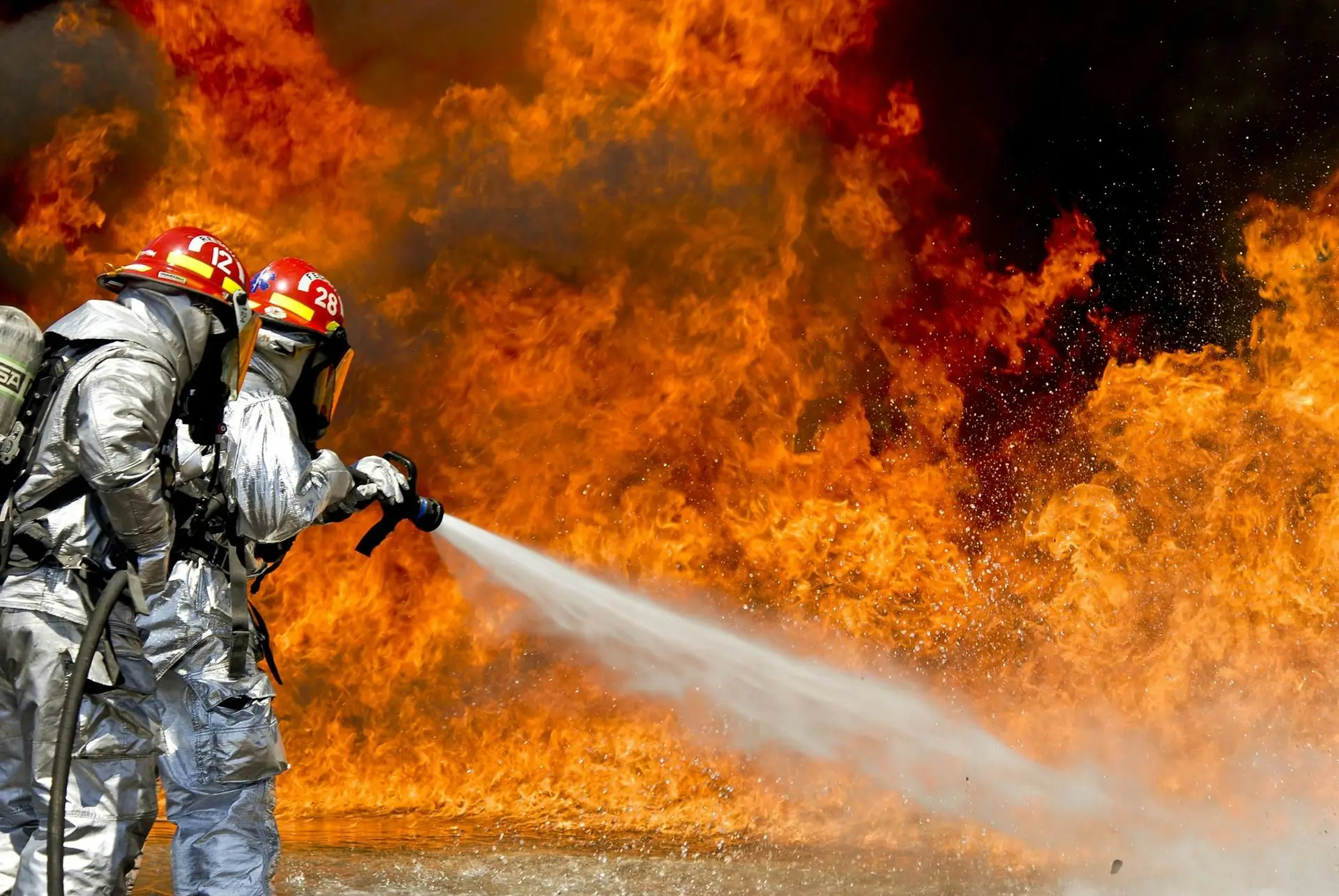 Two firefighters putting out a huge fire with water.