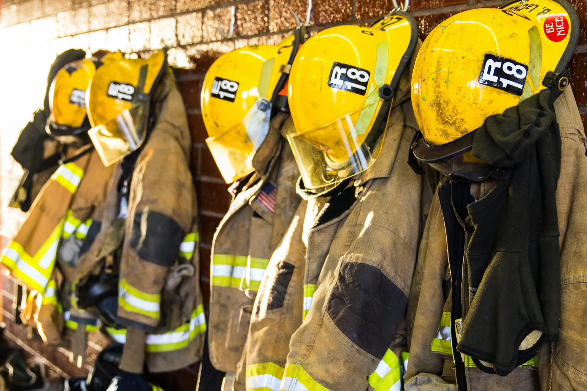 5 bunker gear also known as firefighter's suits are hanged along with the yellow helmets.