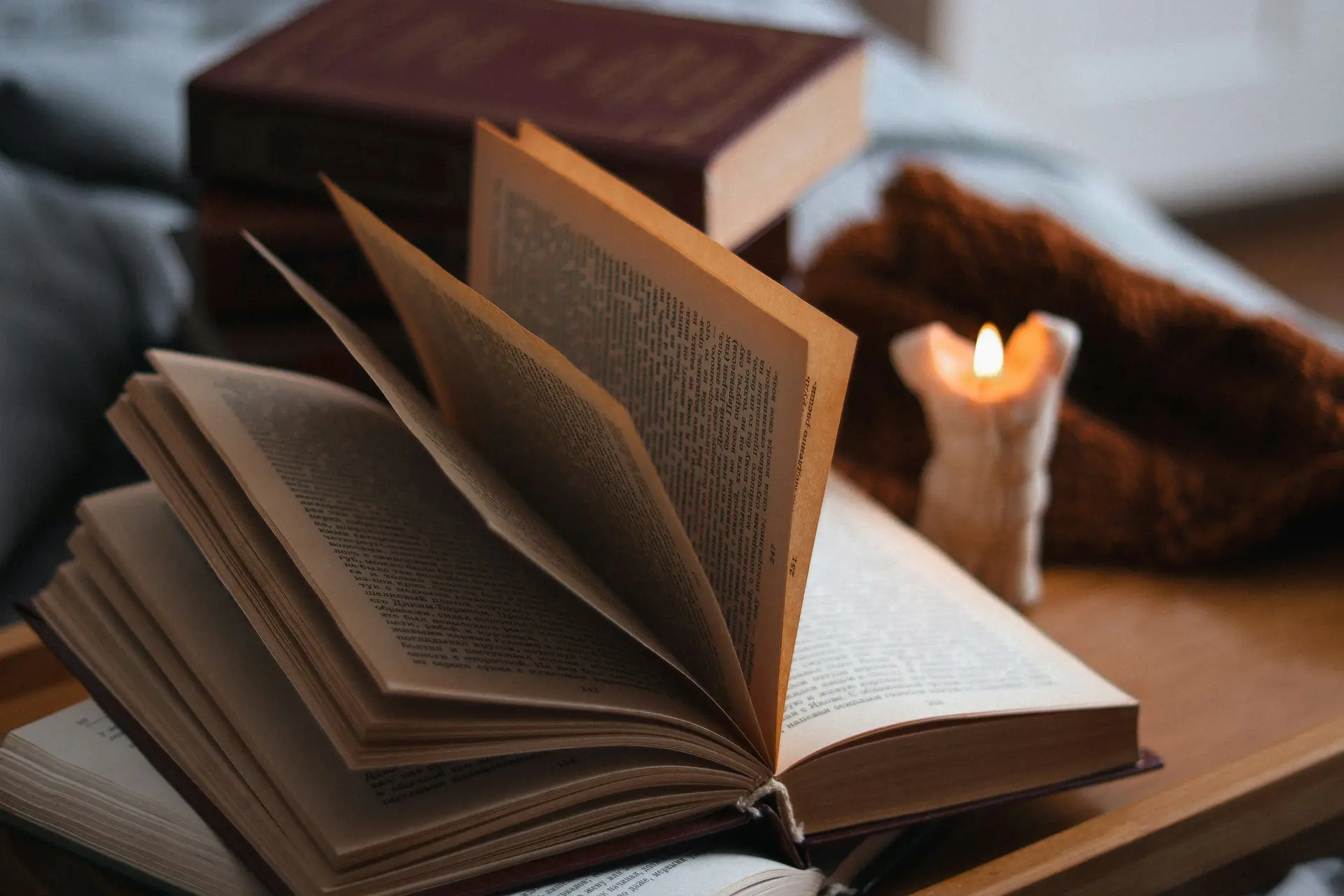 An open book sitting on top of a table next to a lit candle.