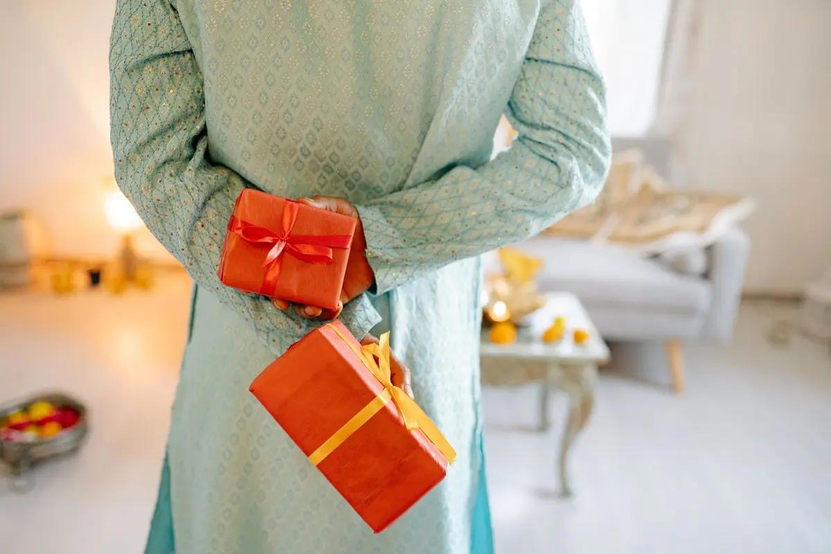A man in traditional attire holds gift boxes during a festive celebration indoors.