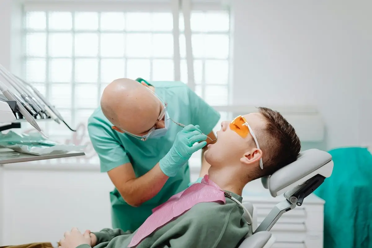 A dentist operating on a patient in his chamber. The patient is wearing uv protection glasses.