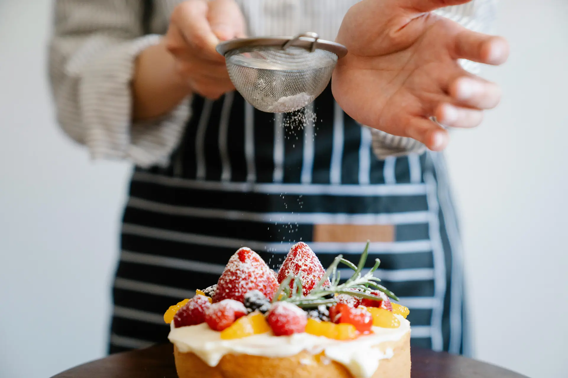 A woman adding finishing touch to a strawberry cake.