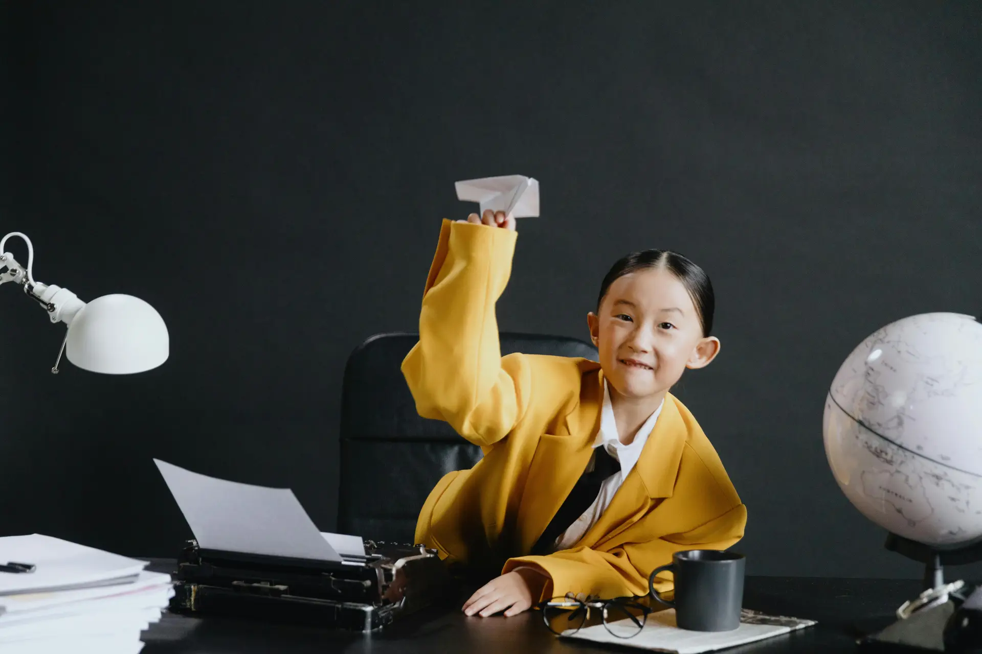 Asian girl in yellow suit holding paper-made plane in hand.