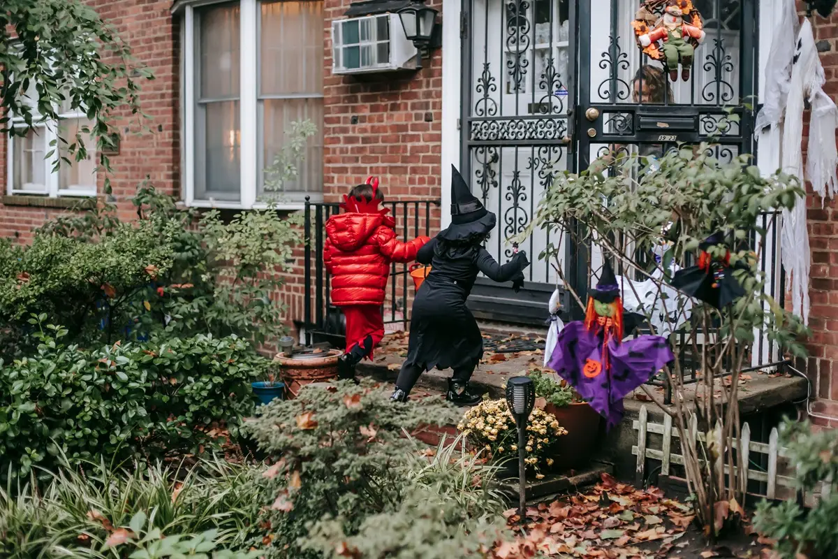 Two kids in devil and witch costumes celebrate Halloween with trick or treating.