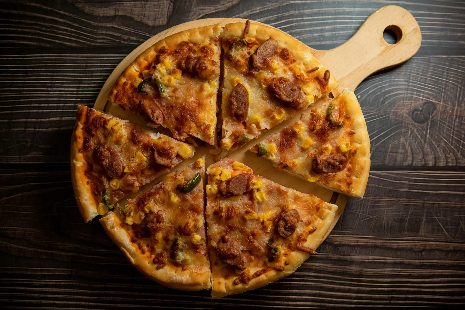 A baked sausage pizza on a wooden pizza tray.