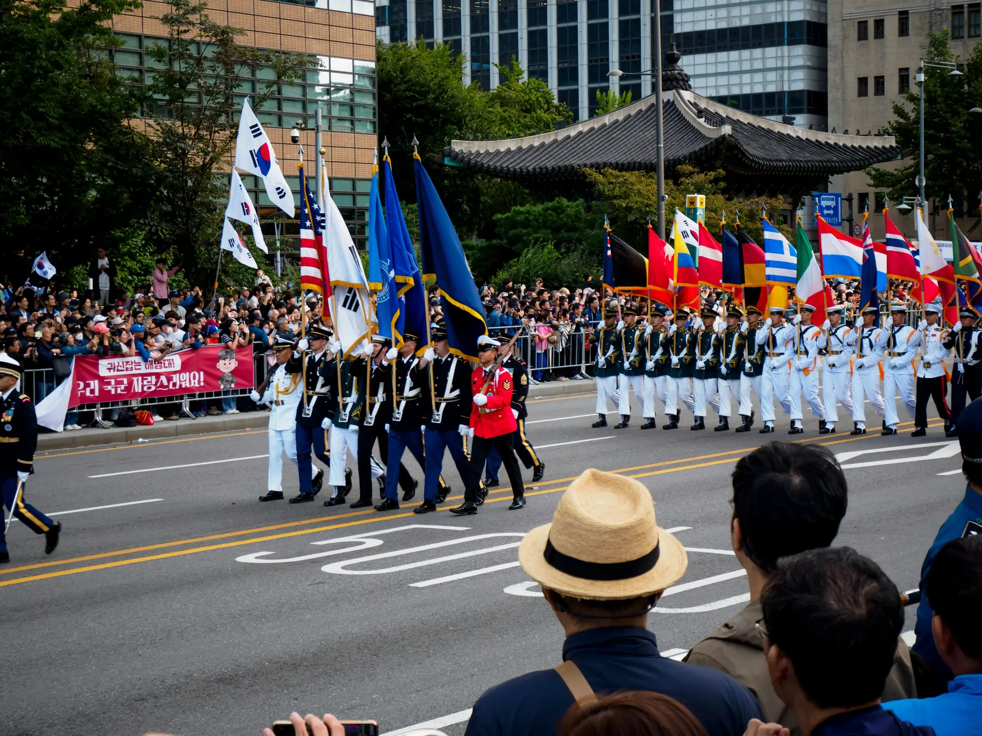 A May Day parade running through the street. People are watching by standing on the street.